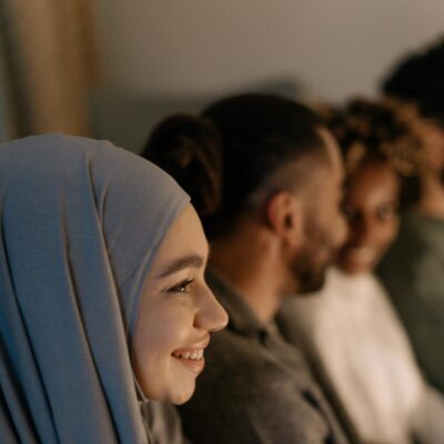 Side profile of a happy woman in hijab with friends indoors, smiling and engaged.